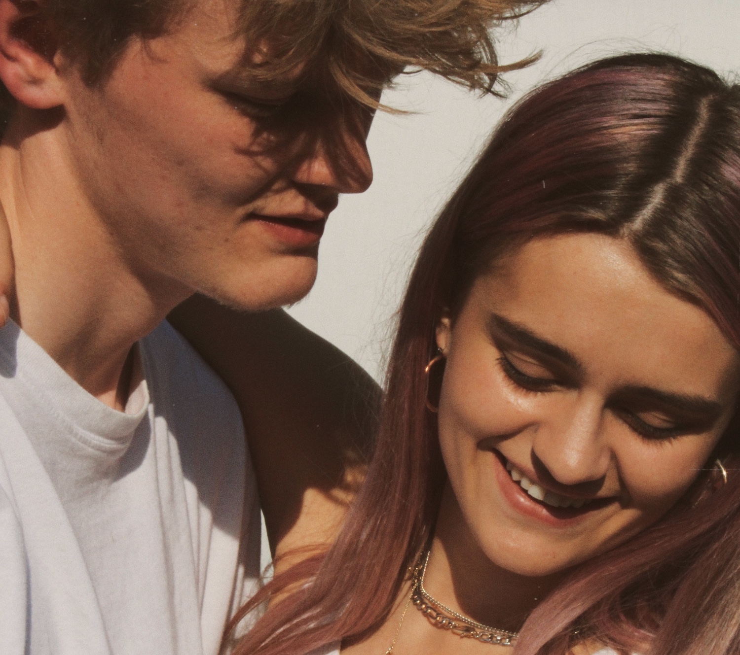 A young man whispers in a young woman's ear, as she smiles and looks coyly downwards